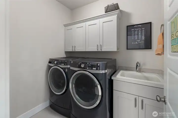 Dedicated laundry room with side-by-side washer and dryer, plus upper cabinetry for added storage and organization.