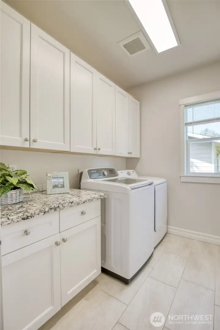Bright and functional laundry room with cabinets for storage and granite counter space to keep things organized.