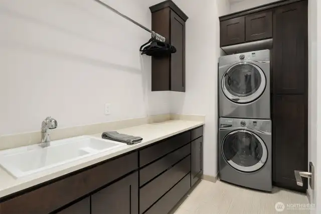 Laundry room with sink cabinets and stacked Whirlpool Duet washer and dryer