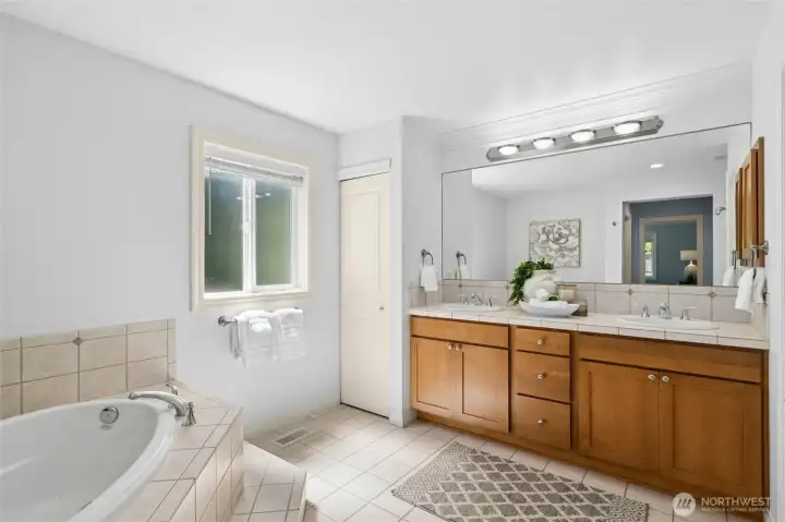 Spacious bath with dual sinks, soaking tub, tile floor and a linen closet.