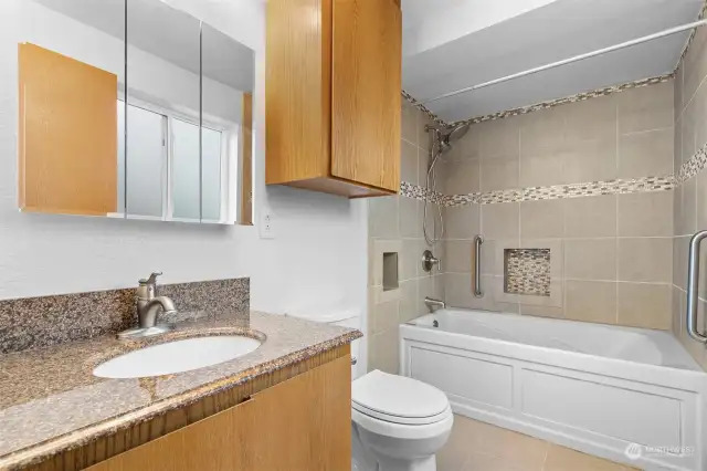 Custom tiled shower/tub combo with built-in shelves, dual shower head, and grab bars.