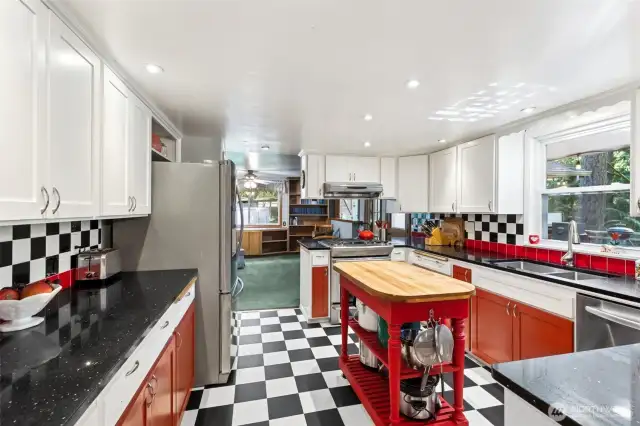 Stylish retro kitchen featuring classis black-and-white chekerboard floors, a gas cooktop, electric stove, and plenty of cabinetry thrroughout.