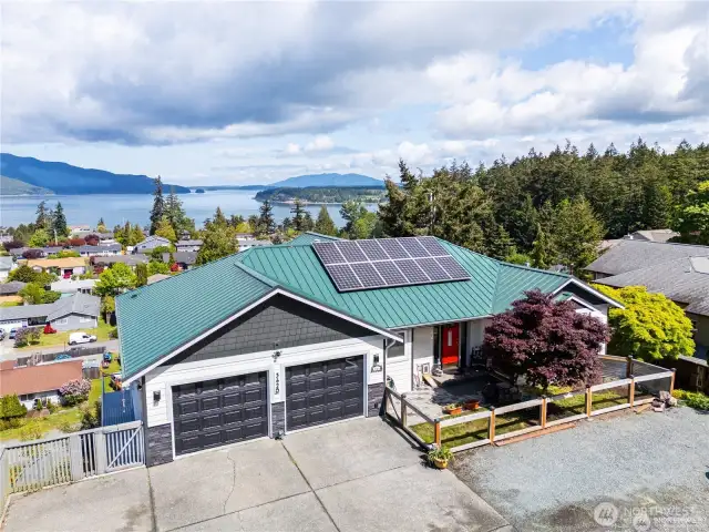 Perched above the neighborhood with sweeping views of the bay and islands, this energy-efficient home features solar panels, a vibrant metal roof, and a welcoming front patio.