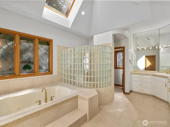 Luxury Primary Bathroom with vaulted ceiling, skylights, soaking tub, and dual sinks.