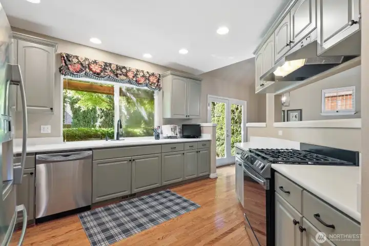The light-filled kitchen features quartz countertops, generous cabinetry, and a beautiful window overlooking the mature landscaping.