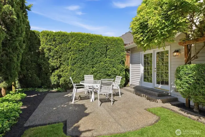 Private patio space framed by lush hedges and greenery, offering a quiet place to relax or dine outdoors.