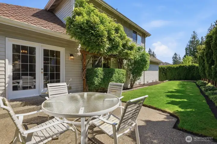 A peaceful backyard setting with a sunny patio, manicured lawn, and mature landscaping designed for easy outdoor enjoyment.