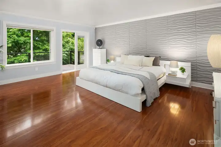 Spacious primary bedroom with rich hardwood floors and textured accent wall Spacious primary bedroom with rich hardwood floors and textured accent wall