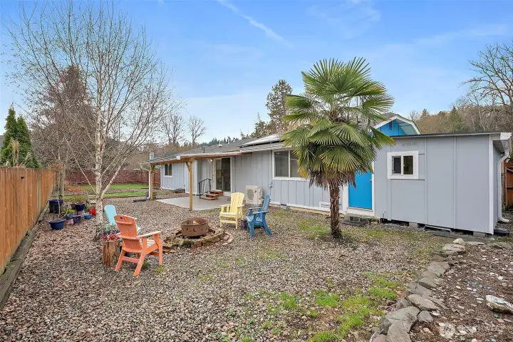 Spacious fully fenced backyard with matured palm tree, campfire space, raised garden beds.