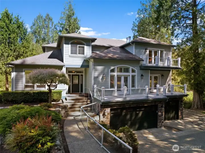 Stately exterior framed by mature landscaping, featuring elevated decks, garage parking, and a welcoming approach.