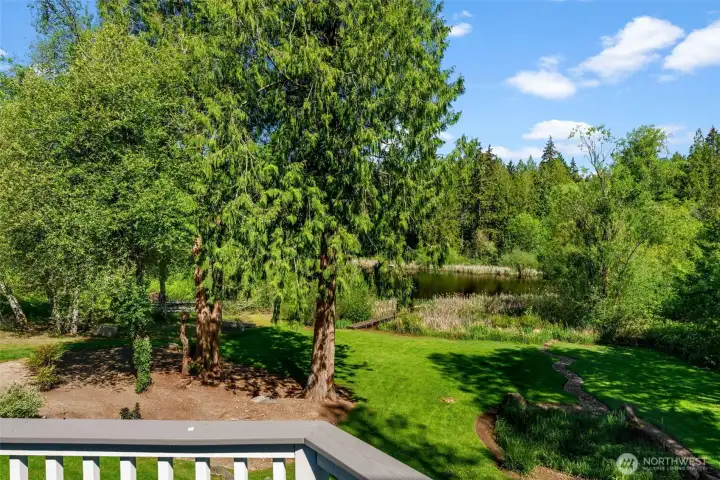 Peaceful backyard setting with mature trees, open lawn space, and tranquil water views from the deck.