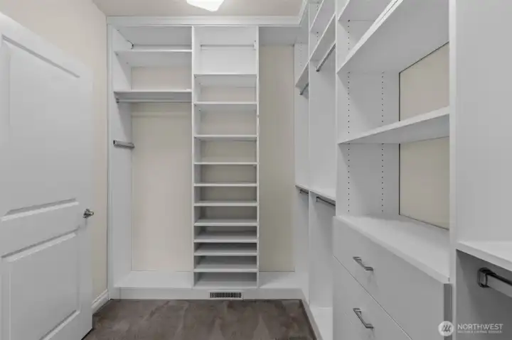 Primary walk-in closet features built-in shelving, drawers, and hanging storage.