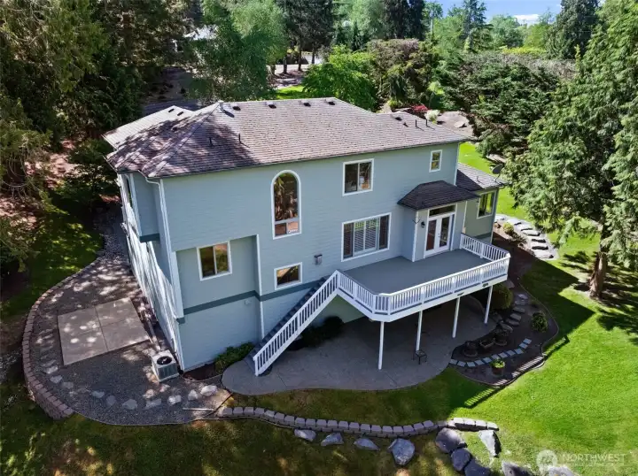 Rear exterior view highlights the home’s expansive deck, landscaped grounds, and surrounding mature trees.
