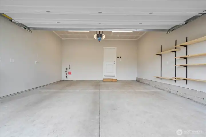 Spacious two-car garage with EV charging capability, storage shelving, and additional workspace potential.