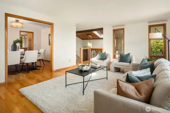A warm and inviting living room featuring rich hardwood floors, a classic fireplace, and an effortless open flow into the dining room beyond — a beautifully connected space bathed in natural light and perfectly suited for both relaxed everyday living and elegant entertaining.