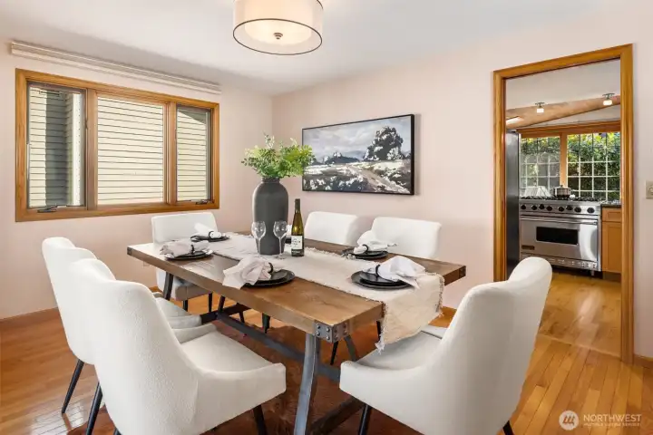A warm and elegant dining room just off the kitchen, bathed in natural light where rich hardwood floors and crisp white furnishings create a timeless, inviting atmosphere — perfectly sized for gatherings and flowing seamlessly into the surrounding living spaces.