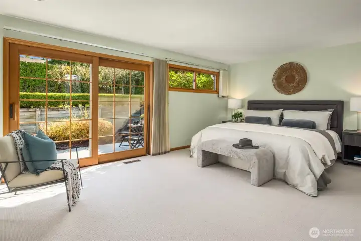 A serene and spacious primary bedroom retreat featuring plush carpet, expansive sliding glass doors that flood the room with natural light and frame lush garden views — a calm, beautifully updated sanctuary perfectly designed for rest and relaxation.