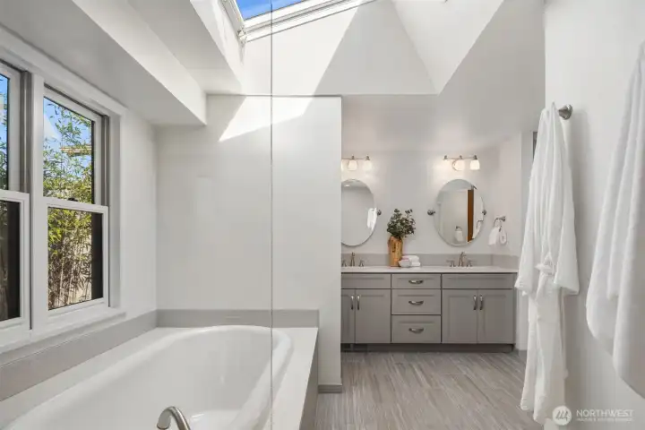 A spa-caliber primary bathroom featuring a luxurious soaking tub beneath a dramatic skylight, elegant dual vanity, and crisp white finishes throughout — a beautifully reimagined space that strikes the perfect balance between indulgence and refined simplicity.
