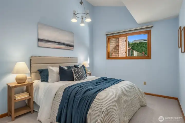 A tranquil and well-appointed second main floor bedroom featuring soft, soothing tones, plush carpet, and a charming window that fills the space with natural light — complete with its own full bathroom, offering comfort and privacy for family or guests alike.