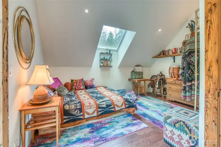 Spacious bedroom with a skylight, reading nook, and sliding doors opening to a deck overlooking the land.