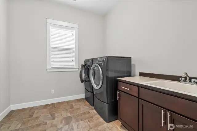 This spacious utility room is as functional as it is bright, thoughtfully designed to simplify everyday tasks. It comes fully equipped with a large washer and dryer, a built-in sink for added convenience, counter space, and ample storage cabinets to keep everything neatly organized. A large wood-wrapped window fills the room with natural light, creating a warm and welcoming workspace that blends utility with style.