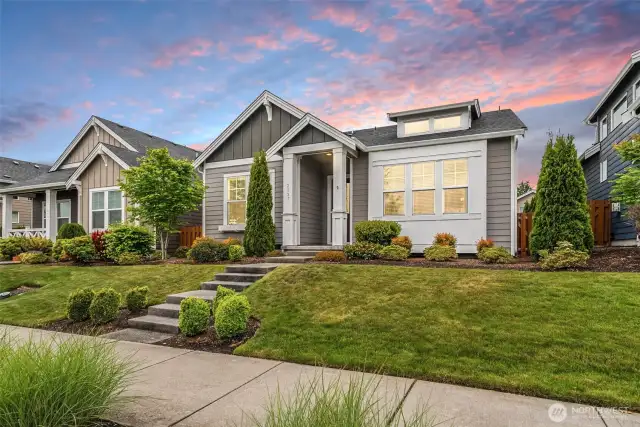 This charming Craftsman-style home commands attention with its striking curb appeal and picture-perfect symmetry. A stately path of symmetrical stone steps leads to the recessed front door, flanked by tall evergreens and vibrant shrubbery that frame the entrance like a regal welcome.
