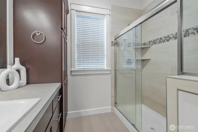 Indulge in spa-like luxury in the stunning primary bathroom, where a grand walk-in tile shower steals the show—adorned with rich ceramic tile accents and enclosed by impressive glass doors that exude sophistication. A spacious double vanity, paired with an additional large vanity, offers abundant space for morning routines and evening unwinding. Thoughtfully designed for both beauty and function, the room also features a dedicated towel closet and a large, wood-wrapped window that bathes the space in natural light while adding timeless architectural charm.