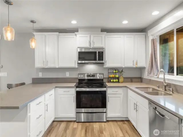 Modern U-shaped kitchen featuring sleek white cabinets, quartz countertops, a peninsula island with seating, and high-end stainless steel appliances—designed for both style and functionality.