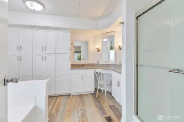 Your updated primary bathroom with two sinks and vanity that accommodates a chair. Large shower at right and soaking tub at left.