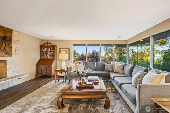Sunlit living room with cozy fireplace and floor to ceiling windows.
