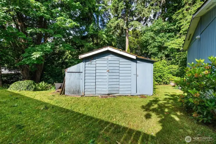The older shed is positioned along the forested edge of the property, with a grassy area in front that gives you flexible outdoor space to use and enjoy.