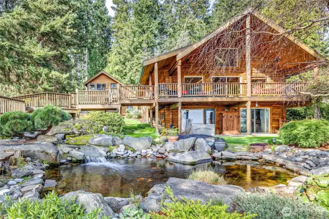The main house and the studio apartment in the background enjoy stunning views of Puget Sound, mountains, and the man-made waterfall and pond.