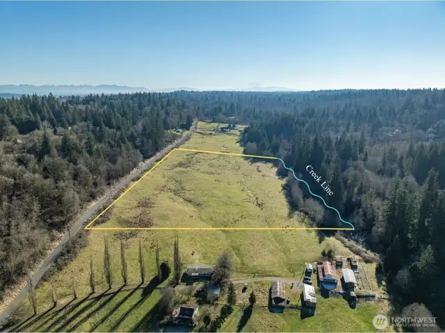 This aerial highlights the full span of the parcel, outlined clearly up to the meandering creek line.