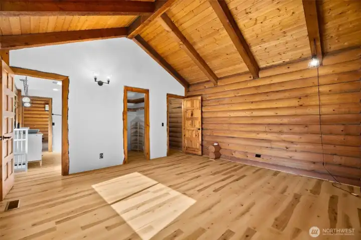 Upper-level bedroom offering sightlines to the walk-in closet and attached bath, beautifully highlighting the natural log walls and warm wood ceilings and custom trim that is throughout the house.