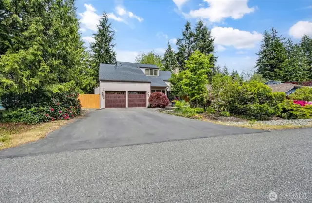 Street view of newer asphalt paved driveway with drainage and new cedar double gate to RV parking space.