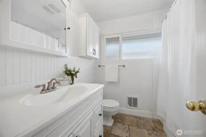 There is a recently updated full bath on the main floor with all white cabinets and fixtures and the stone tile floor similar to that in the kitchen and dining areas.