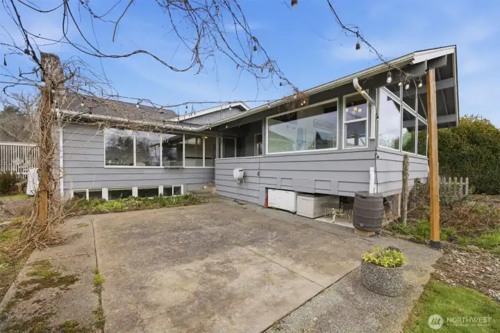 Looking at the large back patio with the herb garden and the wisteria and strung lights. All the downspouts have water catchment systems, too.