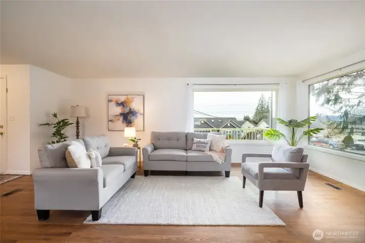 Light, bright and cheery living room with hardwood flooring, open to dining and entry. Great entertaining and living space. (staged)