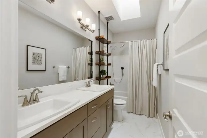Bright and inviting guest bath with dual vanity, skylight above, and a clean, modern design, creating a comfortable and well-lit space.
