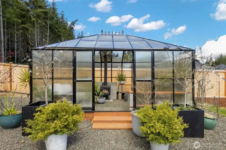 Charming greenhouse retreat complete with a wood-burning fireplace, perfect for year-round growing or curling up with a book in a warm, light-filled sanctuary.