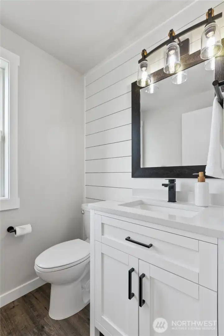 Stylish main-level powder room showcases modern farmhouse finishes with shiplap detail, quartz vanity, and matte black hardware. Stylish main-level powder room showcases modern farmhouse finishes with shiplap detail, quartz vanity, and matte black hardware.