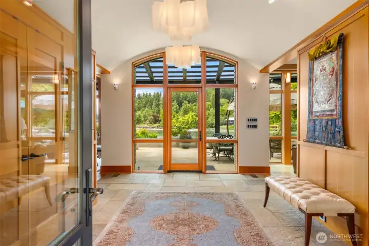 View from the entryway to the water with stone floor tones softened by the curvature of the ceiling and natural wood panels.