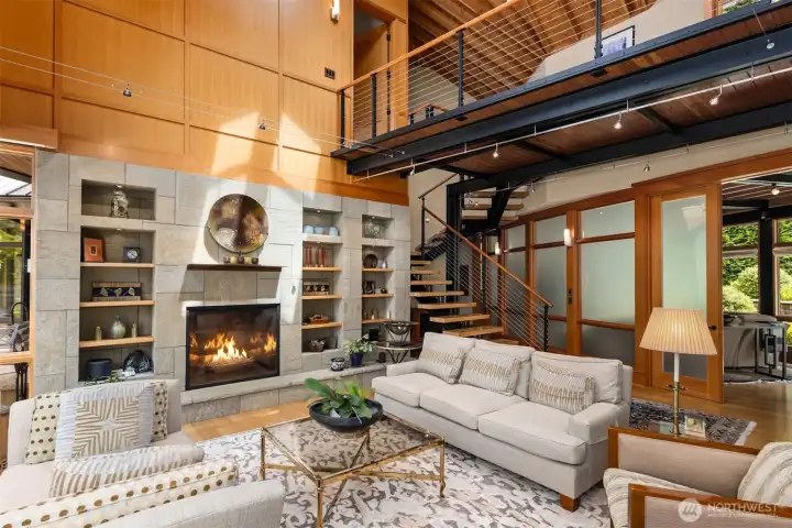 View to the stone surround with art piece lighting, wood and stone shelving. The drama of this two story living room is heightened by the floating staircase to the upper living area and the family room's curved glass wall. The space has the feel of movement.