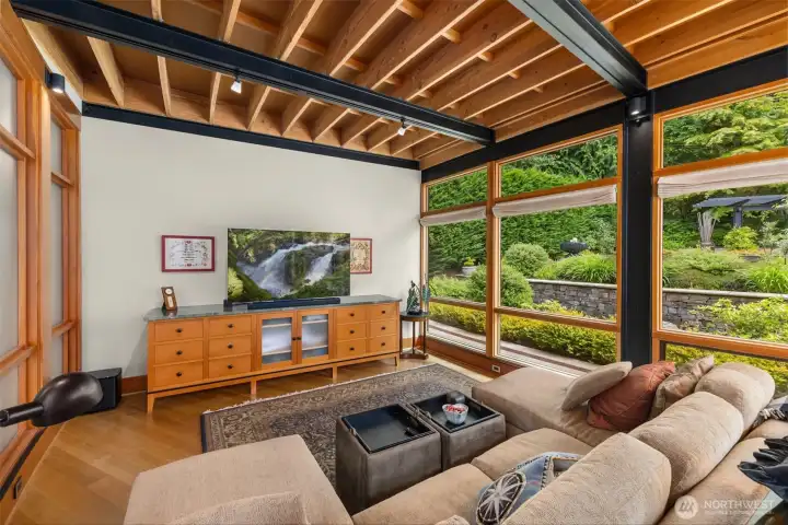 The family room with steel beam, exposed joist engineering, floor-to-ceiling windows framing curated gardens and lawns.