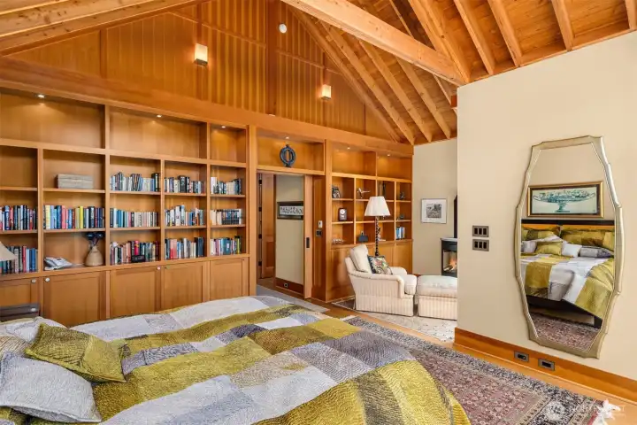 The primary suite is enriched with a wall of built-in shelving and cabinets. View to the slider leading to the walk-in closet and luxury, high-end five piece bath.