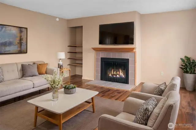 Cozy living room with a wood-burning fireplace, perfect for relaxing evenings. Natural light pours in through the large window facing the courtyard, and built-in shelving adds convenient storage and display space.