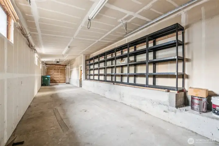 3 car tandum garage with high ceilings, shelving and tall doors at each end.