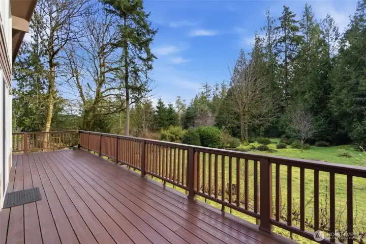 An expansive deck stretches gracefully from the front of the home, offering unobstructed views over rolling vineyards and lush garden space.