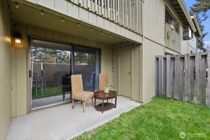 Covered Patio - with storage room, partial privacy fence to the right and a glimpse of the green grass in front of patio.
