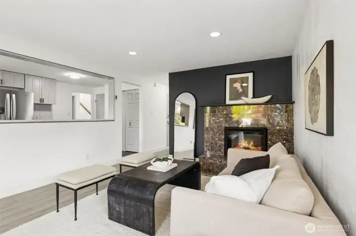 Open-concept living room at 4612 N 21st St, Tacoma, WA, showcasing a modern gas fireplace with marble surround, designer décor, recessed lighting, and a spacious pass-through window connecting the living area to the updated kitchen. This North Tacoma home offers contemporary style, bright natural light, and a seamless layout perfect for everyday living and entertaining.